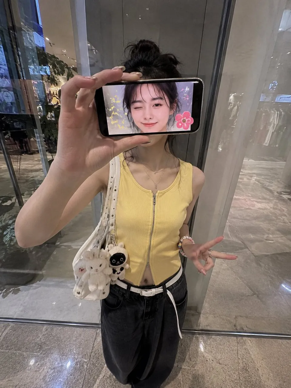 She wears a fitted sleeveless yellow zip-up top, loose black